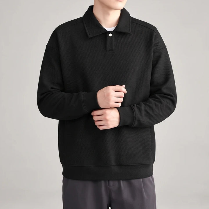 Man wearing a black long-sleeve polo sweatshirt with a textured diagonal stripe pattern, white button, and ribbed cuffs.