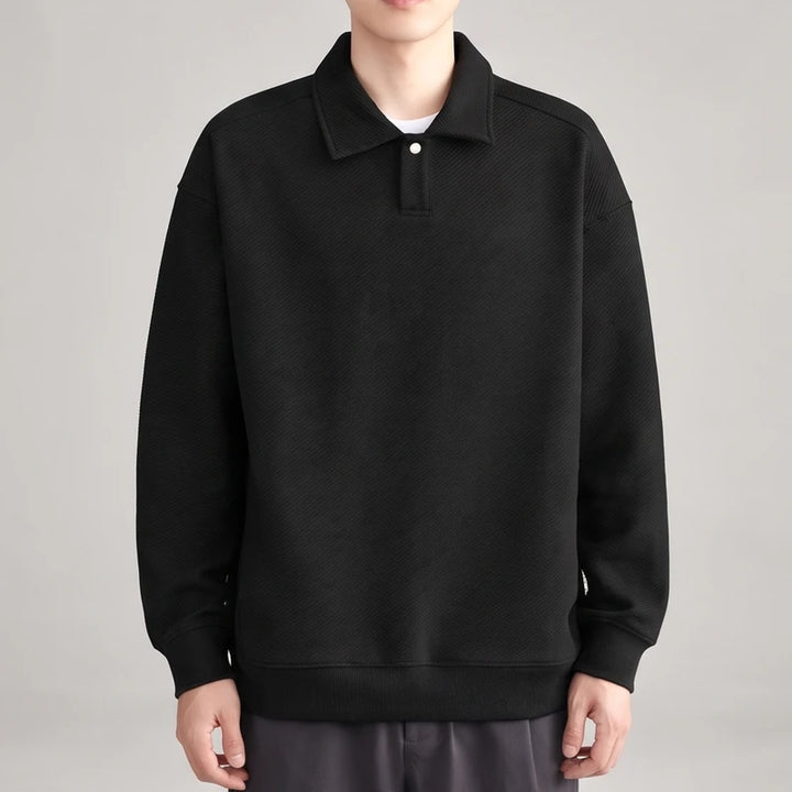 Man wearing a black long-sleeve polo shirt with a single white button on the placket, featuring a subtle diagonal ribbed texture.