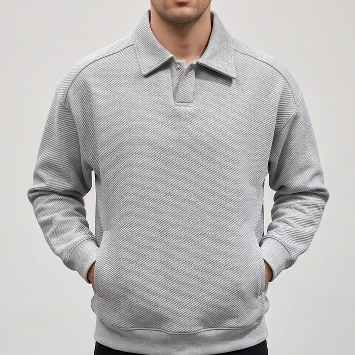 Man wearing a light gray long-sleeve polo sweatshirt with a diagonal ribbed texture and a buttoned placket, hands in front pockets.
