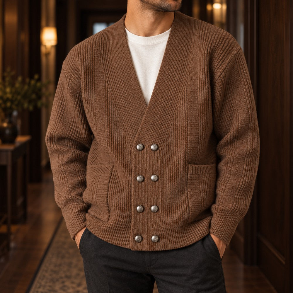 Man wearing a brown ribbed knit double-breasted cardigan with silver buttons, over a white tee, standing indoors.