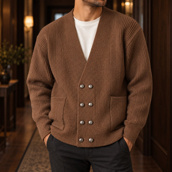 Man wearing a brown ribbed knit double-breasted cardigan with silver buttons, over a white tee, standing indoors.