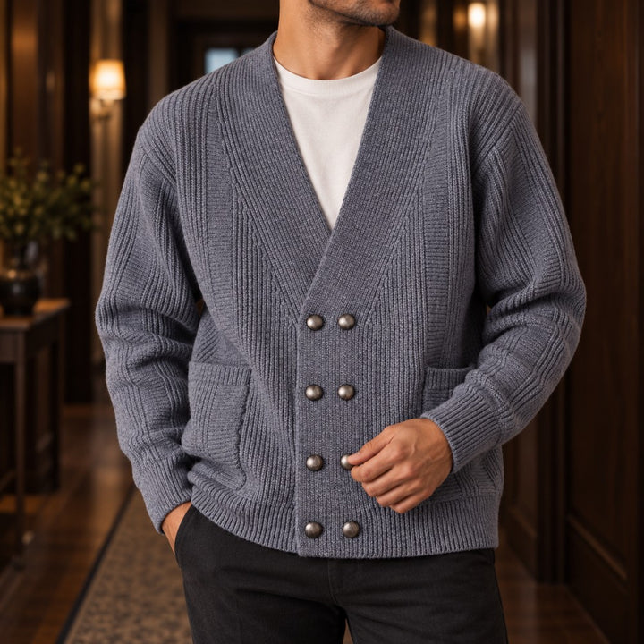 Man wearing a gray ribbed knit double-breasted cardigan with eight antique silver buttons and patch pockets, standing indoors.