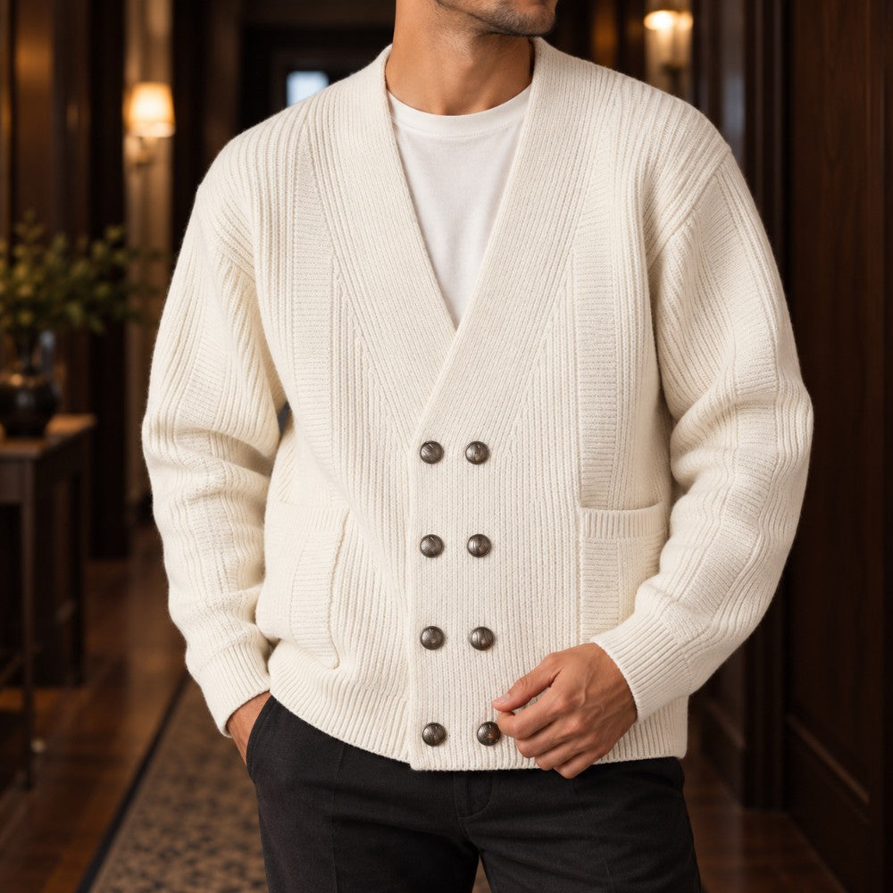 Man wearing a cream ribbed knit double-breasted cardigan with eight dark buttons and two front pockets, standing in a hallway.