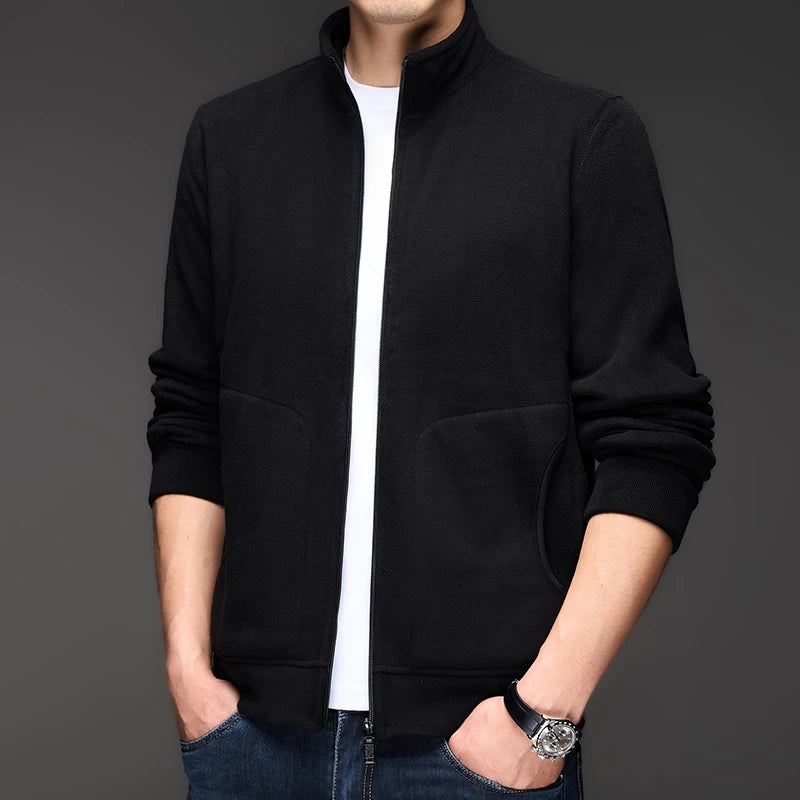 Man wearing a black fleece zip-up jacket over a white t-shirt, standing with hands in pockets.