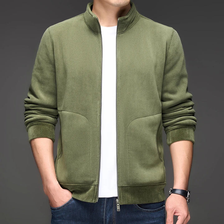Man wearing a dark green textured zip-up jacket with a stand-up collar, ribbed cuffs, and side pockets.