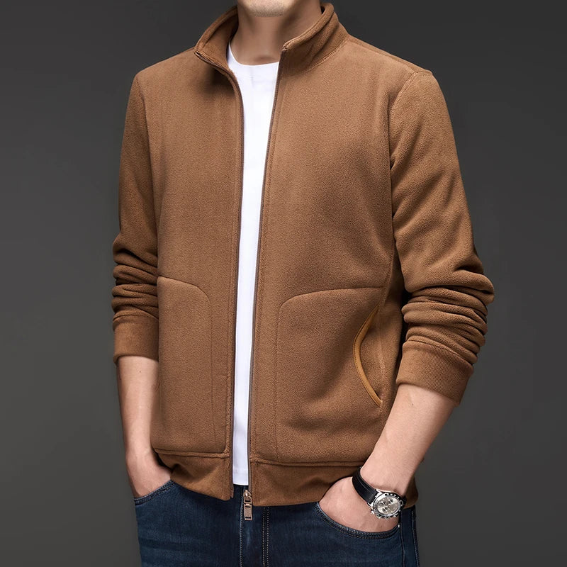 Man wearing a brown fleece zip-up jacket with a stand collar, white shirt, and dark jeans with hands in pockets.