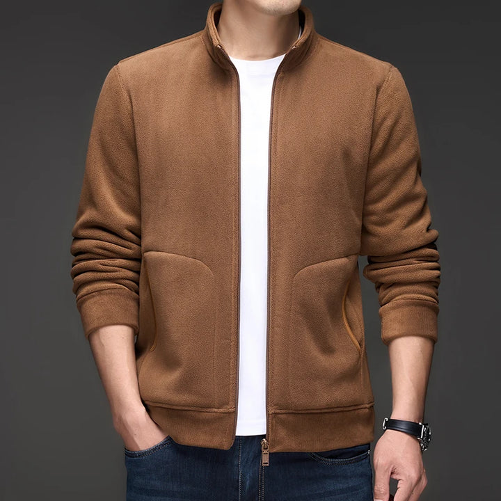 Man wearing a brown fleece zip-up jacket with a white shirt underneath, standing with hands in pockets.