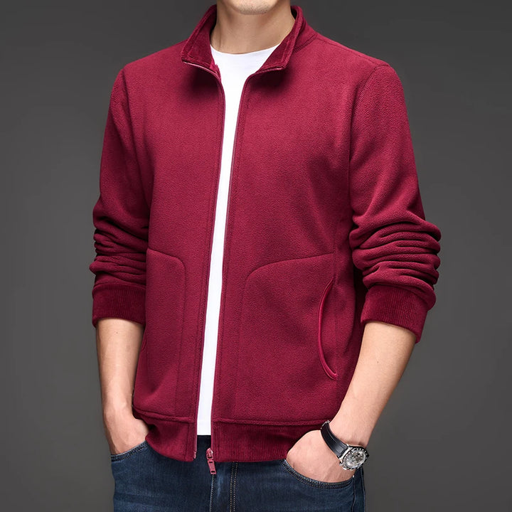Man wearing a burgundy fleece zip-up jacket with side pockets and a ribbed hem, hands in jeans pockets.