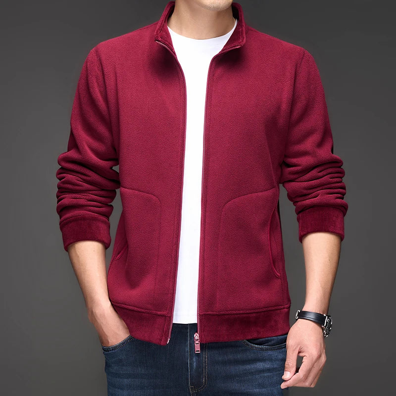 Man wearing a dark red fleece zip-up jacket with ribbed cuffs and hem, over a white tee, standing with hands in jeans pockets.