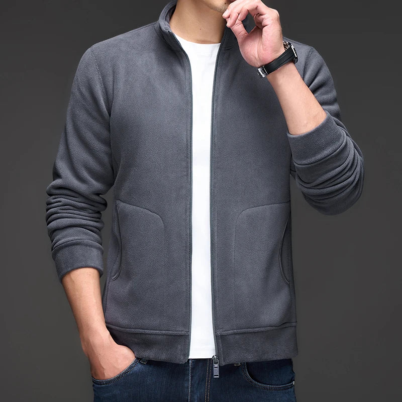 Man wearing a dark gray fleece zip-up jacket with a stand collar, ribbed cuffs, and front pockets over a white tee.