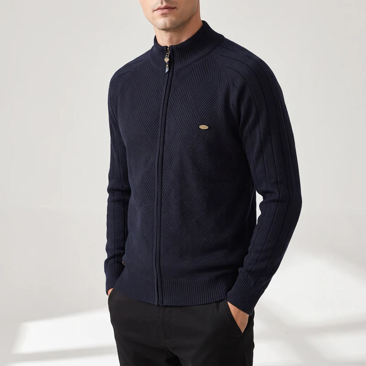 Man wearing a dark navy zip-up knit sweater with a stand collar, unique chest texture, and gold zipper.