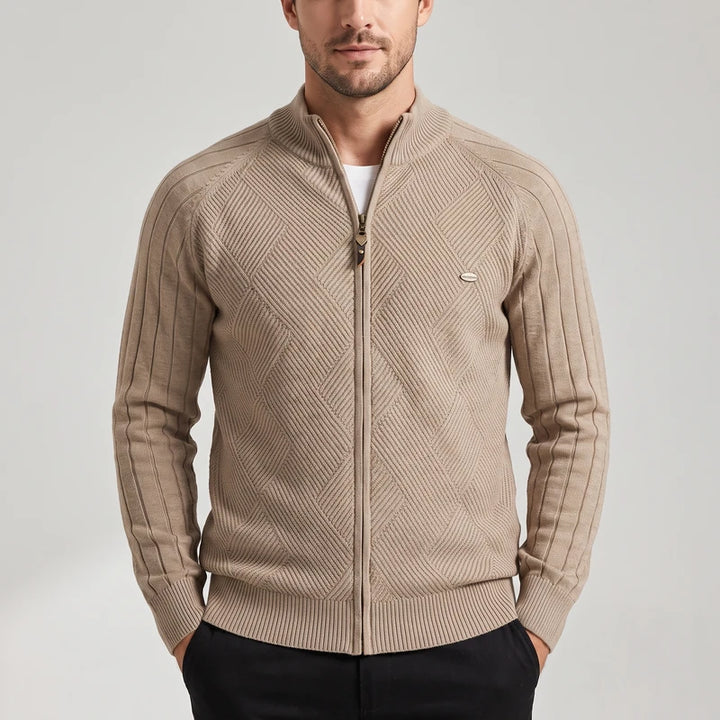 Man wearing a beige knit zip-up sweater with a unique diamond pattern and ribbed sleeves, hands in pockets.