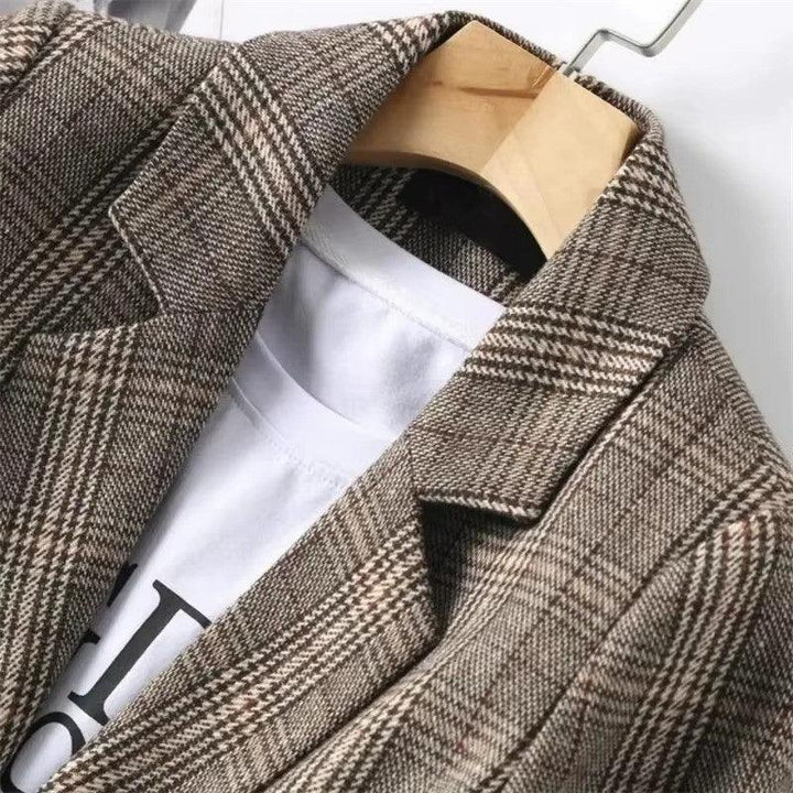 Close-up of a brown and tan plaid blazer with visible texture, hanging on a wooden hanger over a white t-shirt.