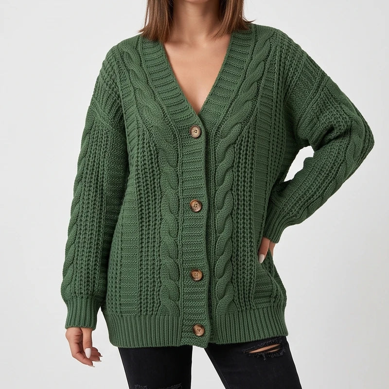 Woman wearing an oversized green cable knit cardigan with a deep V-neckline and six brown wooden buttons over ripped black jeans.