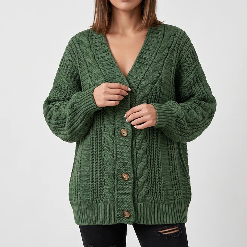 Woman wearing a forest green chunky knit cardigan with cable and waffle textures, holding wooden buttons, over black ripped jeans.