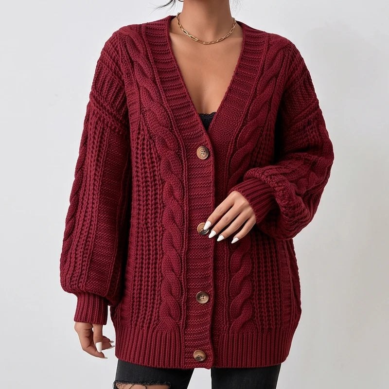 Woman wearing a dark red, chunky knit oversized cardigan with large cable patterns, brown buttons, and puffy sleeves.