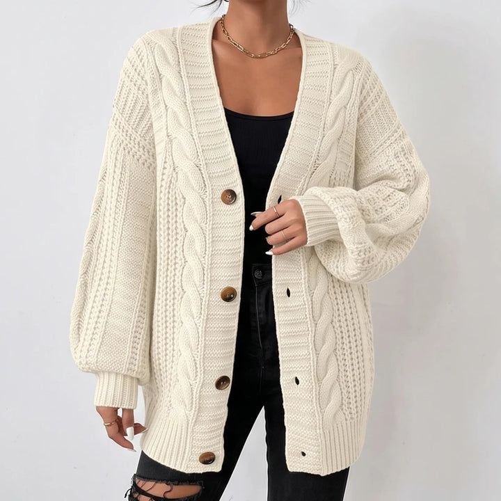 Woman wearing a cream oversized cable knit cardigan with brown buttons, paired with a black top and ripped black jeans.