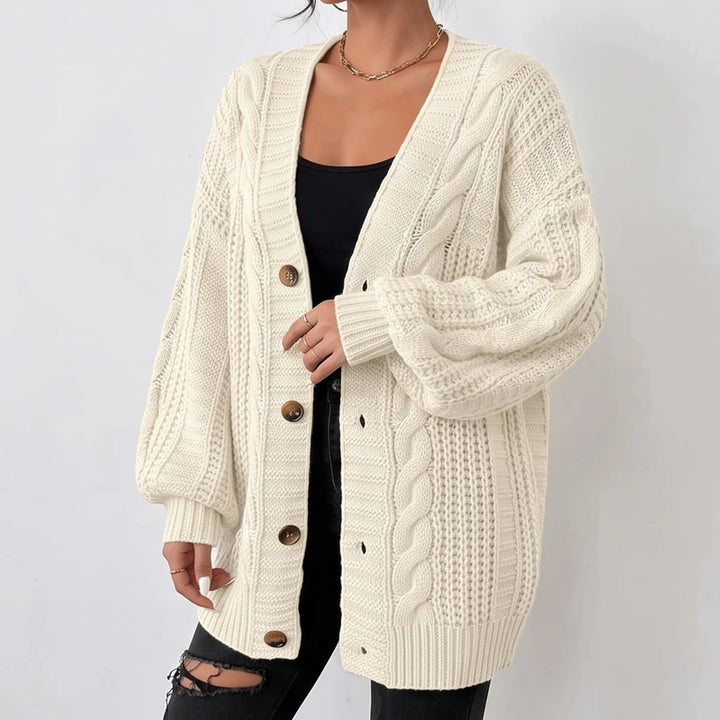 Woman wearing an oversized cream-colored cable knit cardigan with large brown buttons over a black tank top and ripped black jeans.