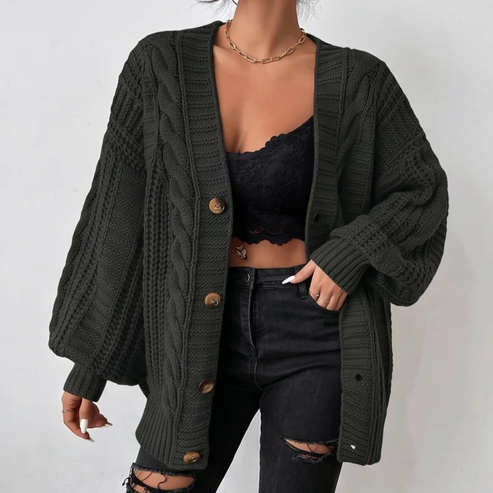 Woman wearing an open dark green cable-knit cardigan with brown buttons over a black lace bralette and ripped jeans.