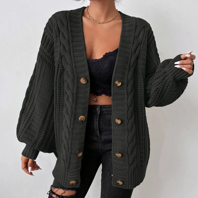 Woman wearing an open dark green cable knit oversized cardigan with large brown buttons over a black lace bralette.