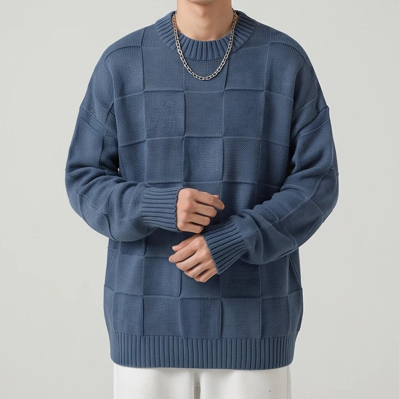 Man wearing an oversized indigo blue knit sweater with a textured checkerboard pattern and a ribbed hem, posed against a plain background.