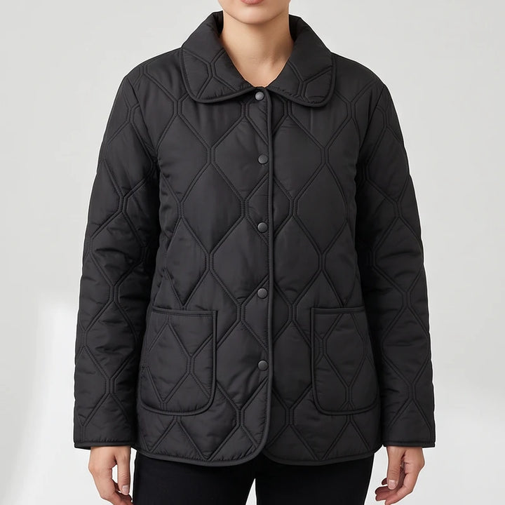 Woman wearing a black quilted jacket with a pointed collar, snap buttons, and two patch pockets on a white background.
