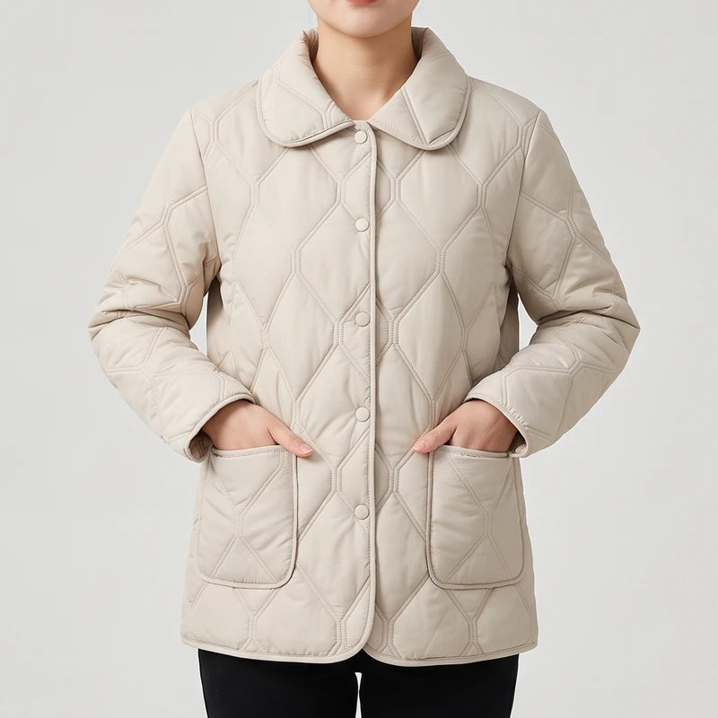 Woman wearing a light beige quilted jacket with a rounded collar, button front, and hands in patch pockets.