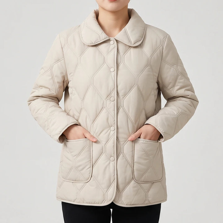 Woman wearing a light beige quilted jacket with a rounded collar, button front, and hands in patch pockets.