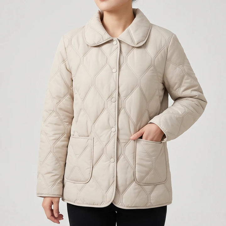 Woman wearing a beige quilted jacket with a rounded collar, button front, and two large front pockets.