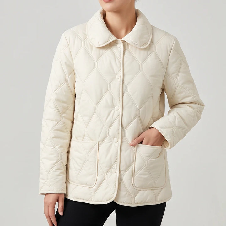 Woman wearing a cream quilted jacket with a round collar, front buttons, and a patch pocket.