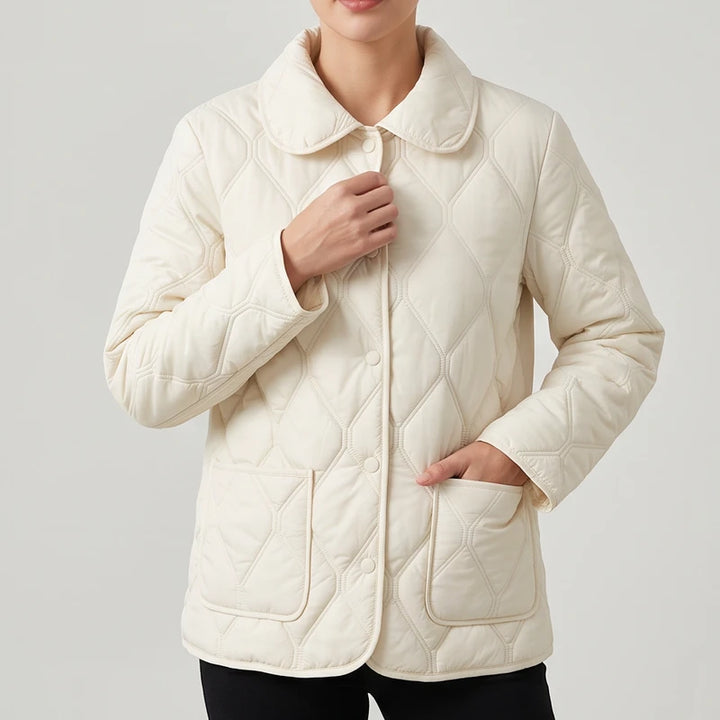 Woman wearing a cream quilted jacket with a round collar, button front, and two front patch pockets.