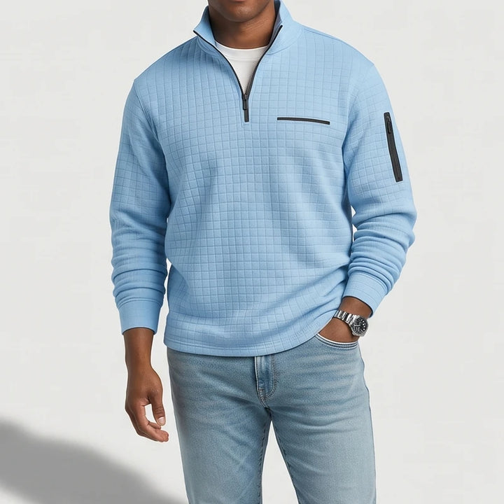 Man wearing a light blue textured quarter-zip with a black zipper, chest pocket, and sleeve pocket, paired with jeans.