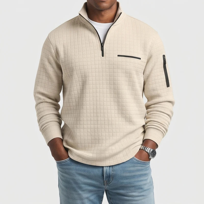Man wearing a cream-colored, textured quarter-zip pullover with black zippers and a collar, paired with light blue jeans.