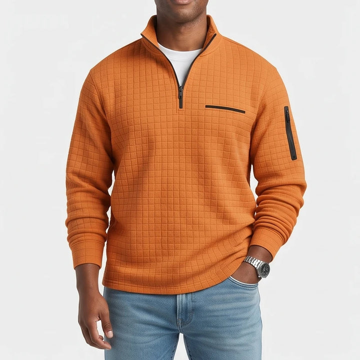 Man wearing a textured orange quarter-zip pullover with a black chest pocket and sleeve zipper, and light wash jeans.