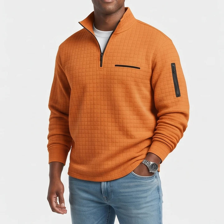 Man wearing a textured orange quarter-zip pullover with a black zipper, chest pocket, and sleeve pocket, paired with jeans.