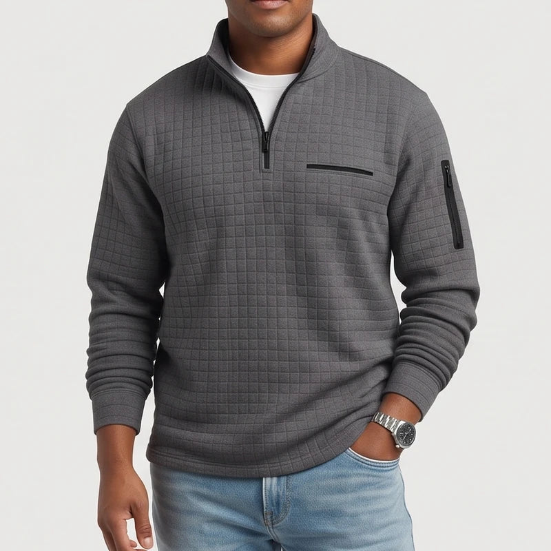 Man wearing a dark gray quilted quarter-zip pullover with black zippers, a chest pocket, and an arm pocket.