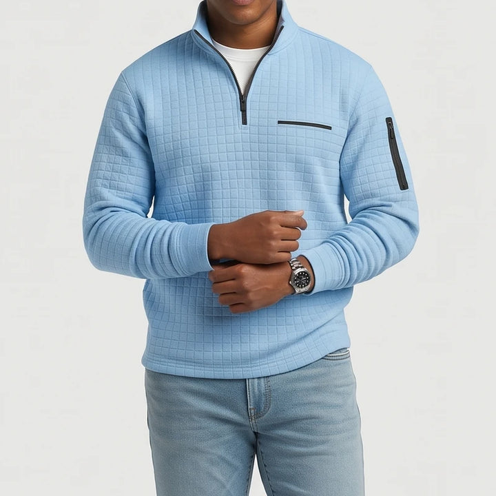 Man wearing a light blue textured waffle-knit sweater with a black quarter-zip closure and arm pocket, against a white background.