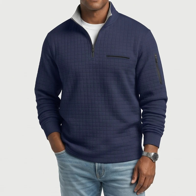 Man wearing a navy blue quilted quarter-zip pullover with a gray collar lining, chest pocket, and arm zipper.