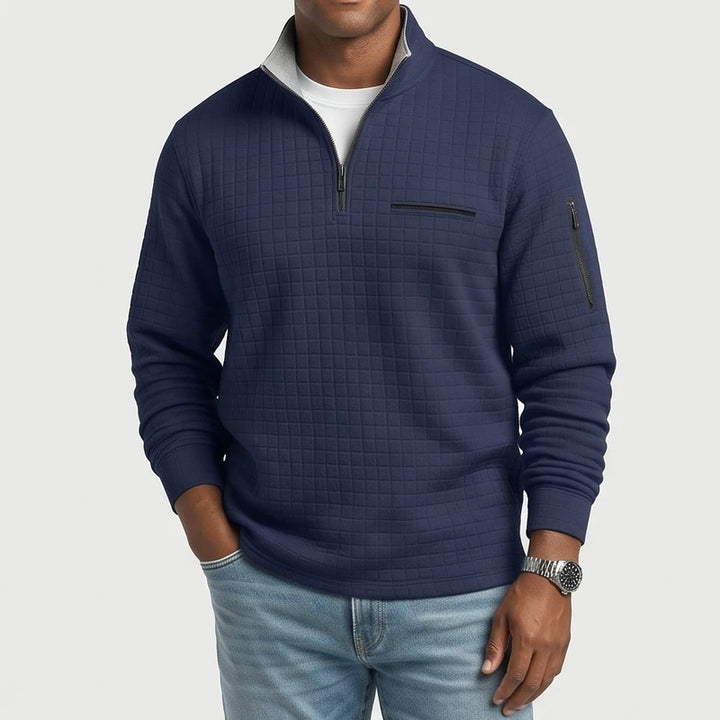 Man wearing a navy blue quilted quarter-zip pullover with a gray collar lining, chest pocket, and arm zipper.