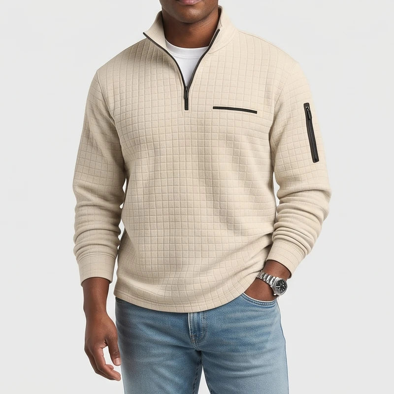Man wearing a beige quilted quarter-zip pullover with black zippers, light blue jeans, and a silver watch.