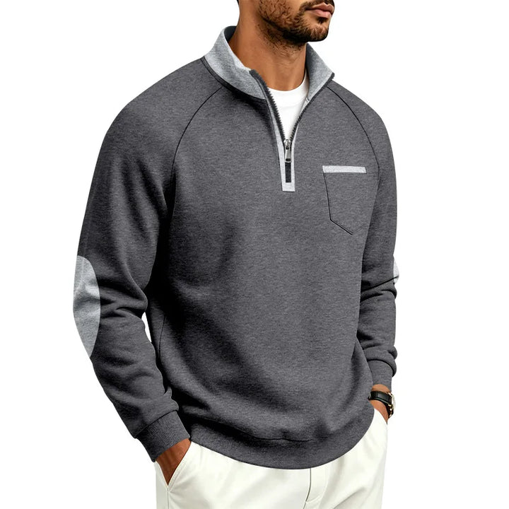 Man wearing a charcoal grey quarter-zip pullover with light grey collar, elbow patches, and chest pocket trim.
