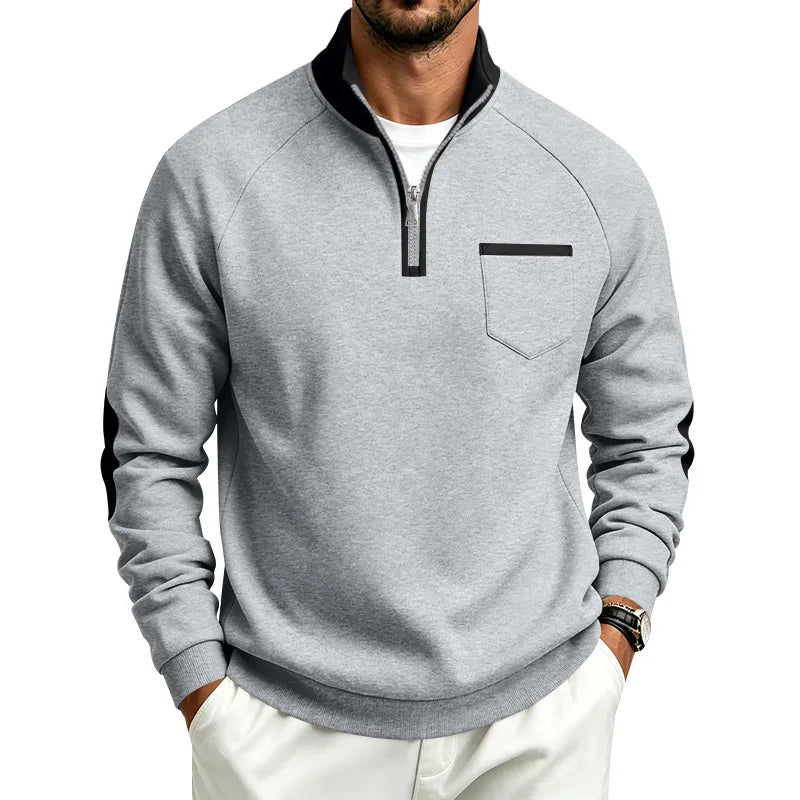 Man wearing a light grey pullover with a black quarter-zip collar, a chest pocket, and black arm stripes.