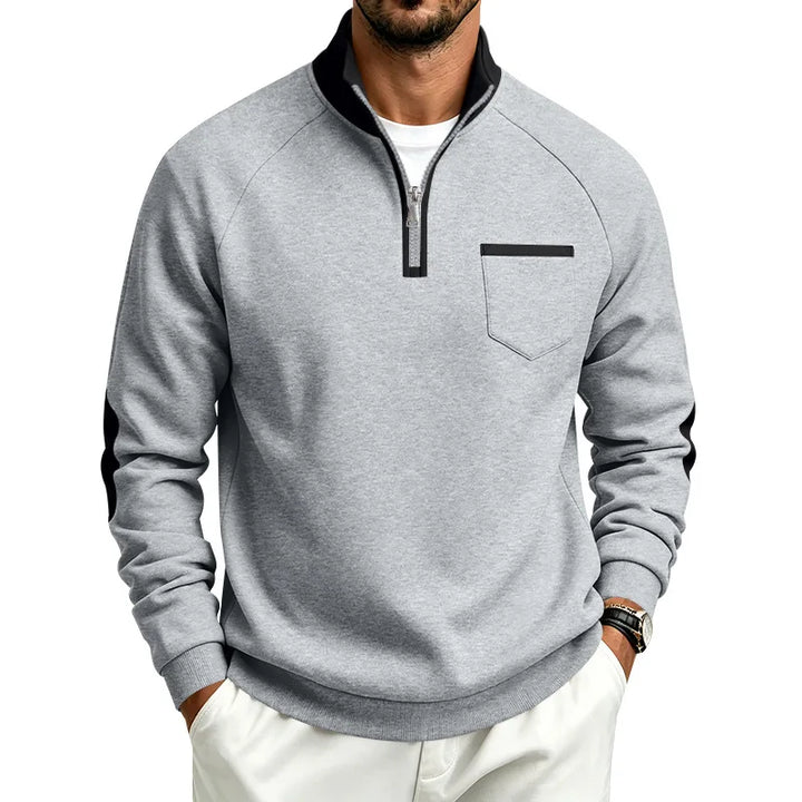 Man wearing a light grey pullover with a black quarter-zip collar, a chest pocket, and black arm stripes.