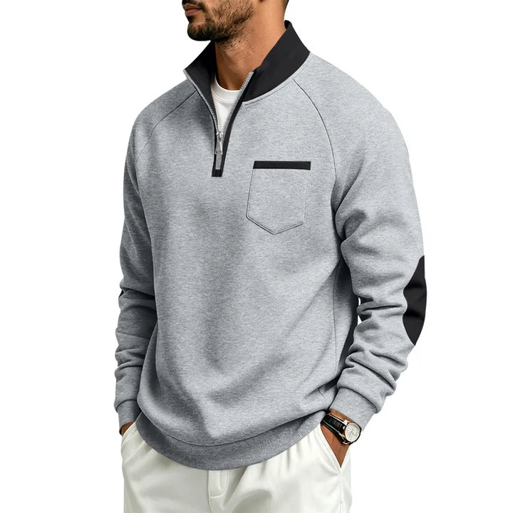Man wearing a heather gray quarter-zip pullover with black collar, black chest pocket trim, and black elbow patches.