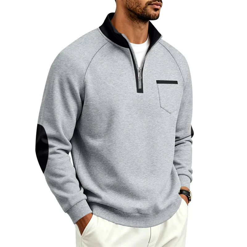 Man wearing a heather gray quarter-zip pullover with black collar, zipper trim, and elbow patches, with hands in pockets.