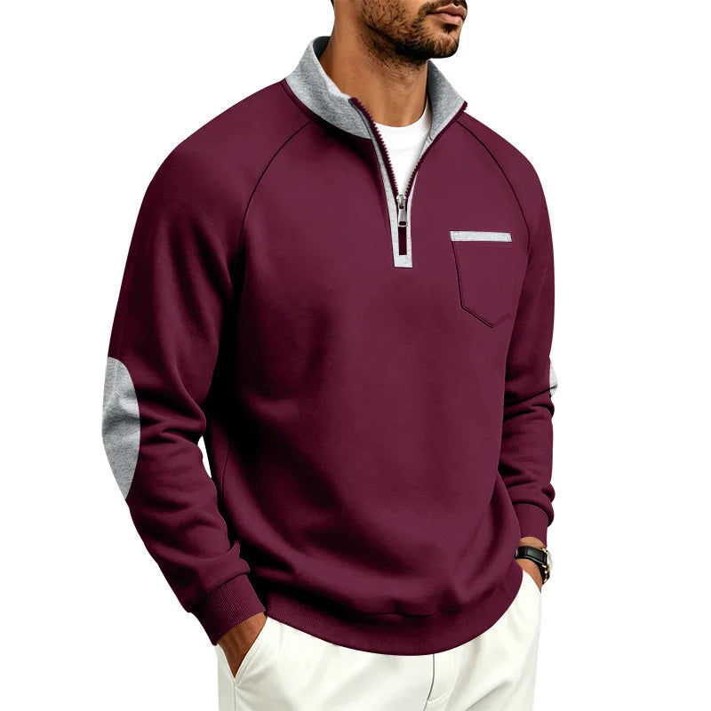 Man wearing a burgundy quarter-zip sweatshirt with a gray collar, chest pocket, and elbow patches, posing against a white background.