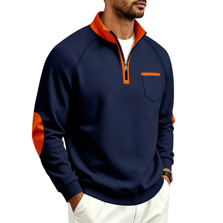 Man wearing a navy blue quarter-zip sweatshirt with an orange collar, zipper placket, pocket trim, and elbow patches.