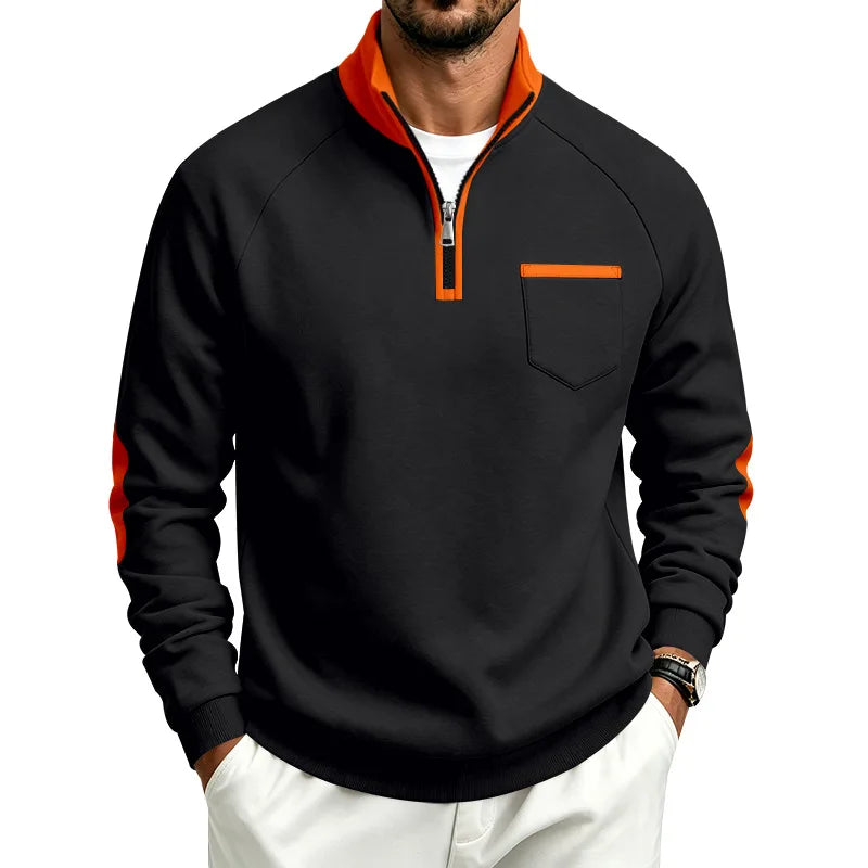 Man wearing a black quarter-zip pullover with orange collar, zipper trim, chest pocket, and arm stripes, hands in pockets.