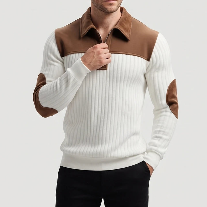 Man wearing a cream ribbed sweater with a brown collar, shoulder panels, and elbow patches, zipping up the front.
