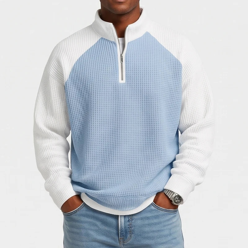 Man wearing a loose-fit, light blue and white waffle knit quarter-zip sweatshirt with raglan sleeves and jeans.